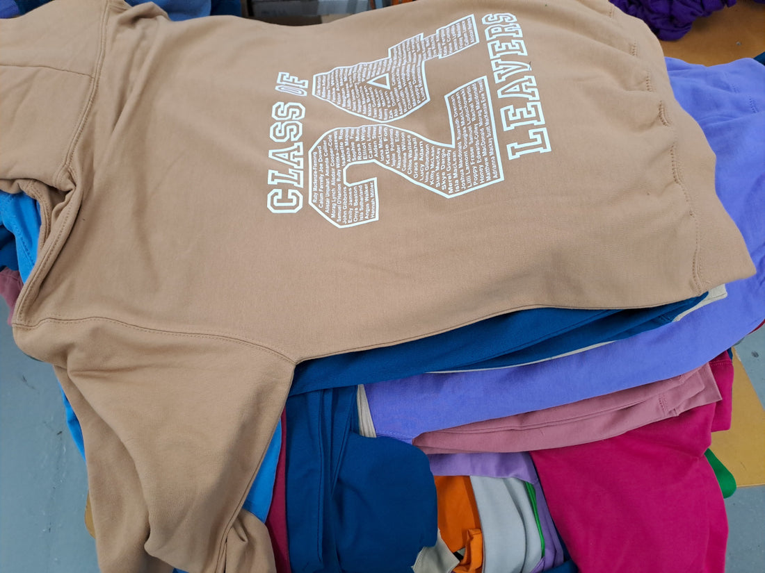 Pile of different coloured leavers hoodies decorated with 24 outline containing pupil names